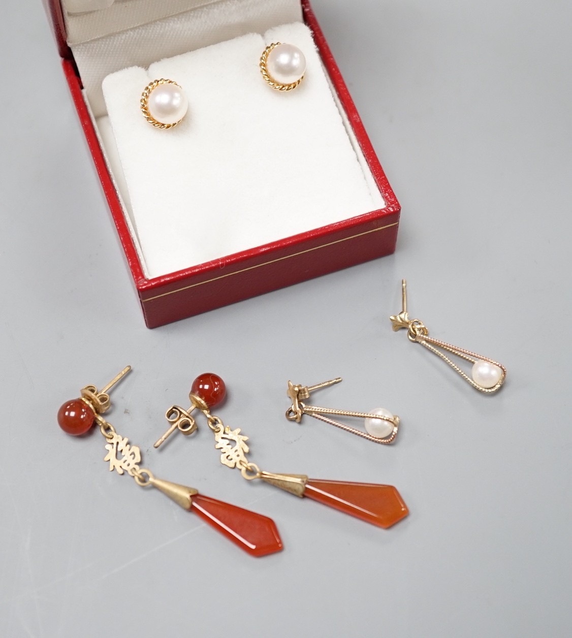 A modern pair of 585 yellow metal and cultured pearl ear studs, a pair of yellow metal and carnelian set drop earrings and a similar pair of cultured pearl earrings.